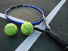 A tennis racket and two tennis balls lay on a court