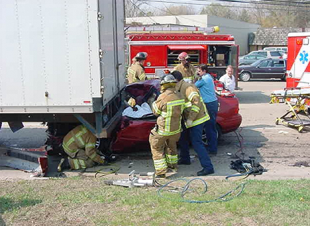 Firemen with car stuck under semi-truck 
