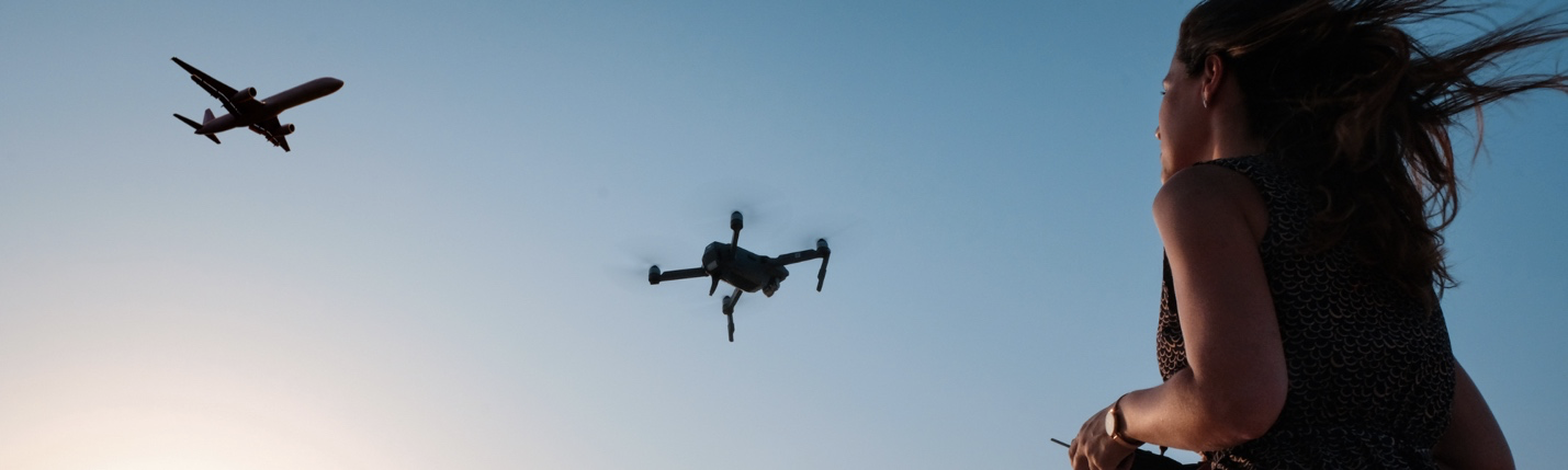 Drone operator looking at their drone in the sky with an airplane in view