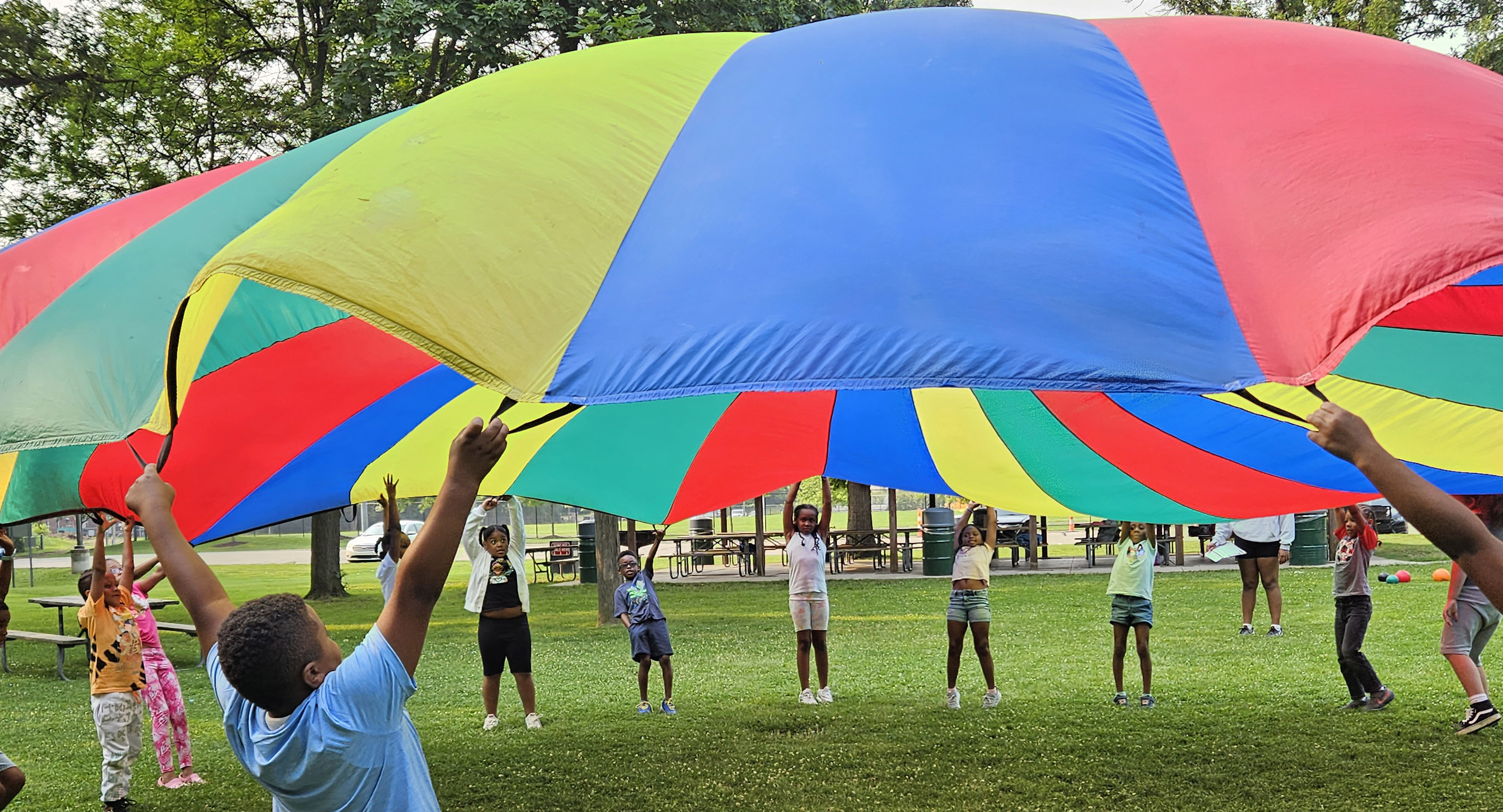 Summer day camp participants play with a large colorful parachute at Civic Center Park.