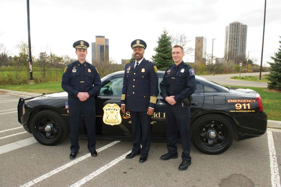 Two police officers and the chief of police in front of a police car.