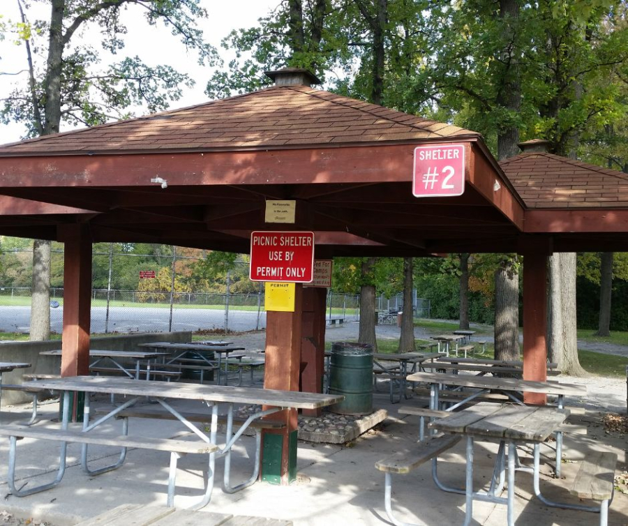 Covered picnic shelter with picnic tables and permit-only signage, surrounded by trees.