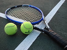 A racket and two tennis balls sit on a court